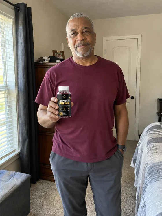 Man holding a bottle of Strong Peak gummies at home